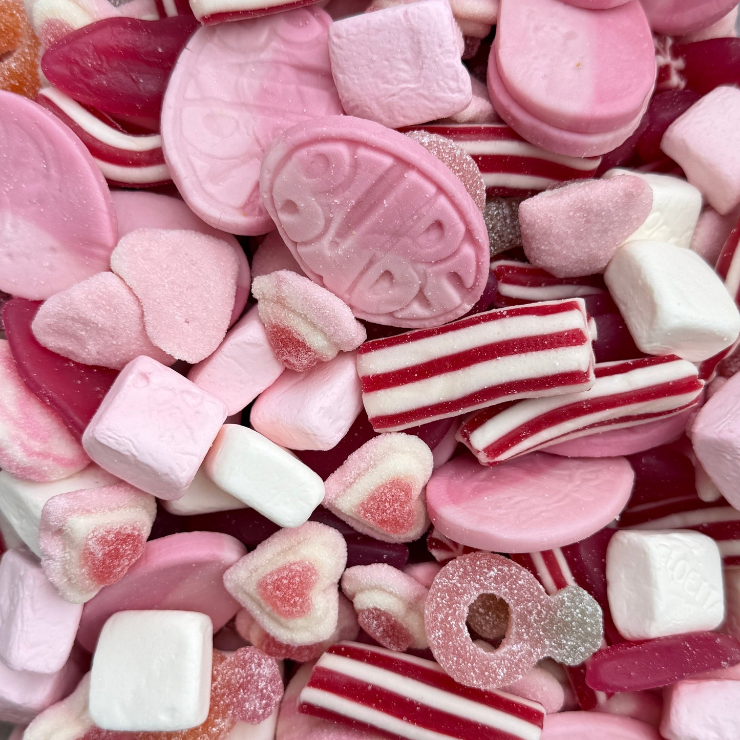 Assorted pink and red candies including heart-shaped and striped pieces.